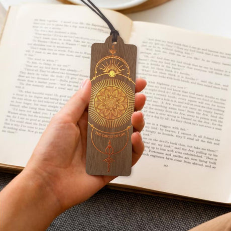 Hand som håller i bokmärke gjord av trä. Motivet på bokmärket är som en mandala. Wooden bookmark - The circle of life från Cozywood - Tidformera